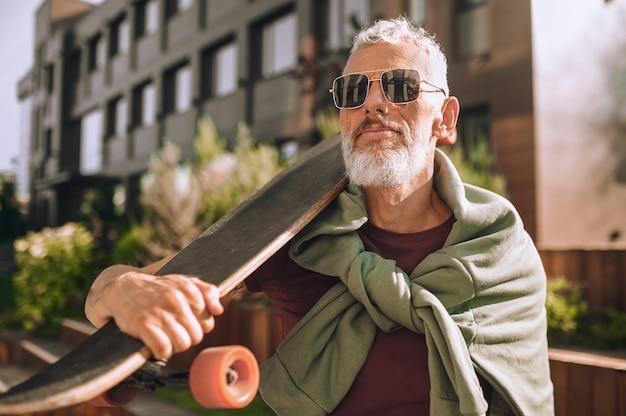 Portrait of a man with a skateboard over his shoulder standing near an office building