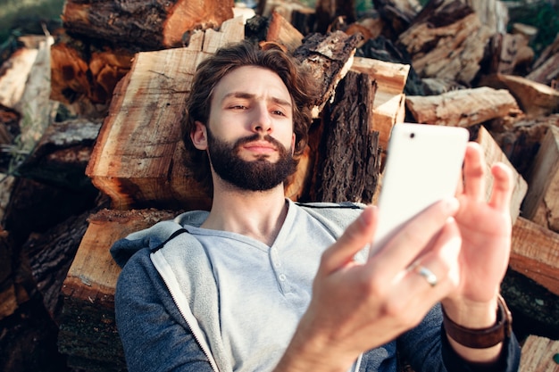 Ritratto di uomo con lo smartphone su una catasta di legna.