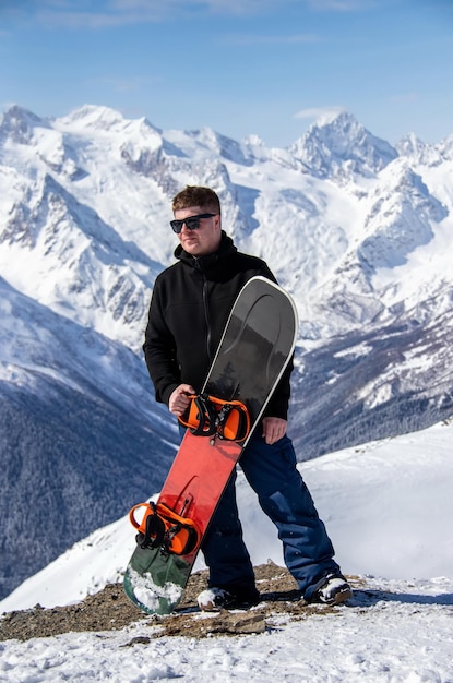 Ritratto di un uomo con lo snowboard in cima a una montagna innevata.