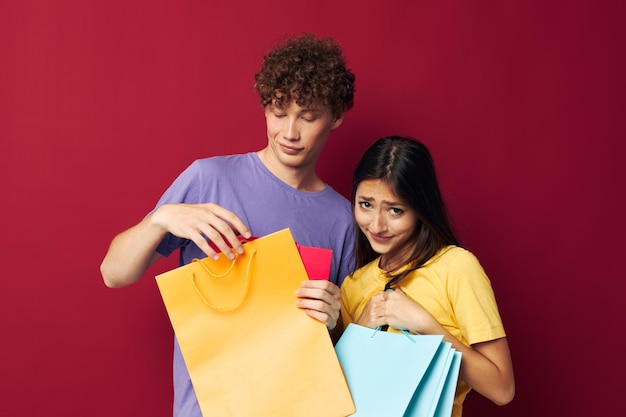 Портрет мужчины и женщины с красочными сумками, делающими покупки весело на красном фоне без изменений