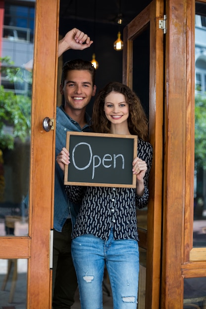portrait of man and woman showing chalkboard with open sign