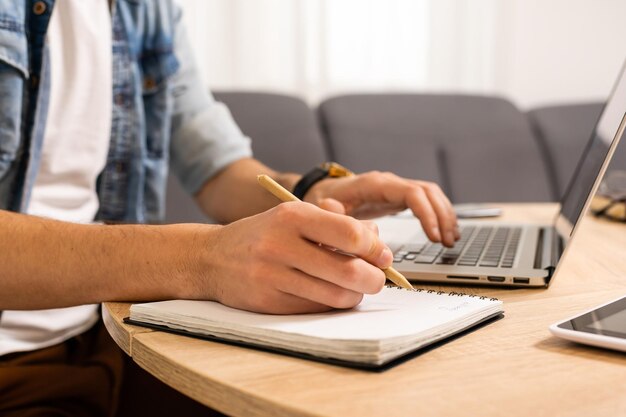 Portrait of a man working at home on some project, he is sitting at a table, drawing ideas on a notebook, with his laptop in front of him.