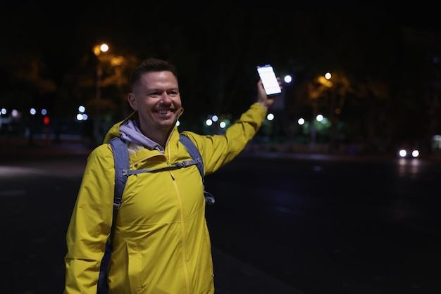 Portrait of man in yellow coat holding mobile phone in hand meeting friends on street in