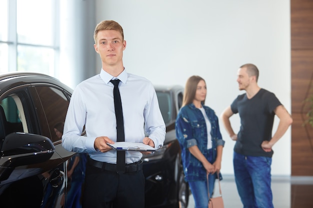 Portrait of a manager in a car dealership against the background of cars and buyers