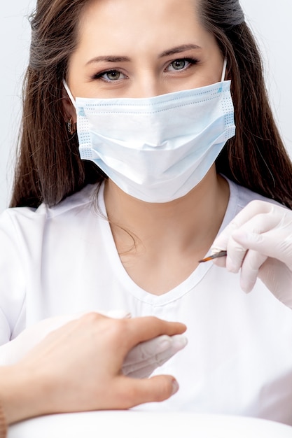 Portrait of manicure master with protective mask working with female customer in beauty salon