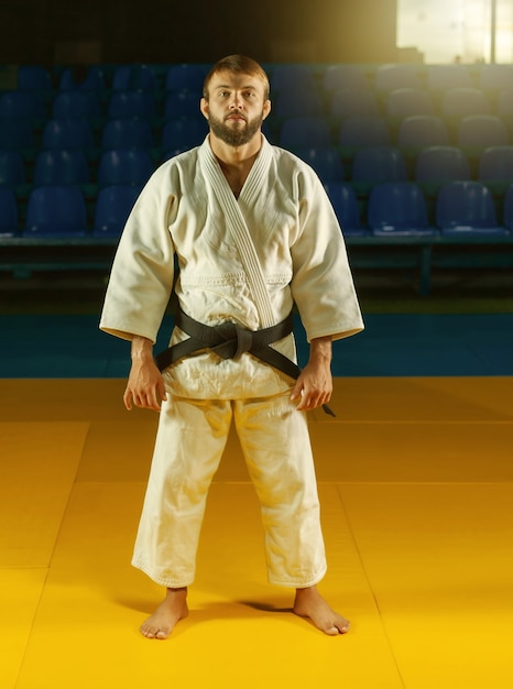 Портрет мастера боевых искусств в белом кимоно с черным поясом в спортивном зале