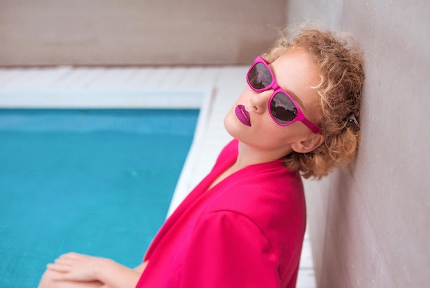 portrait of marvelous stylish redhead curly young woman sitting by the swimming pool