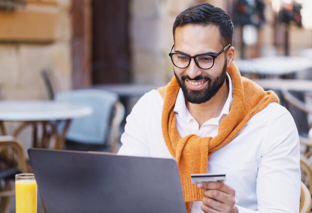 portrait of masculine businessman in smiling and working on laptop while sitting in cafe outdoors