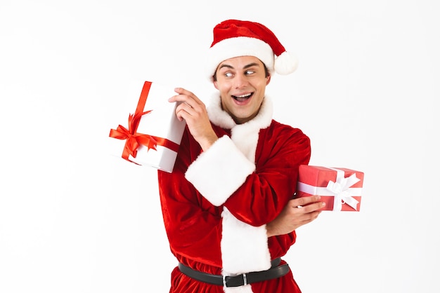 Portrait of masculine man 30s in santa claus costume and red hat holding gift boxes