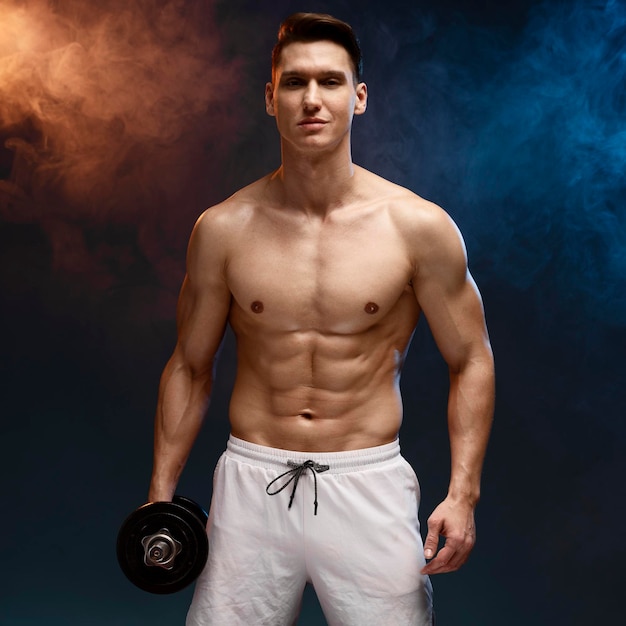 Portrait of masculine young man holding dumbbell isolated on black background