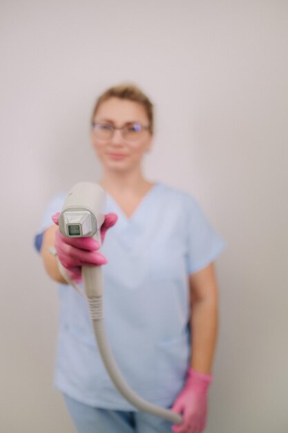 Portrait of the master of laser hair removal a woman in a blue
robe holds a laser hair removal device in her hands