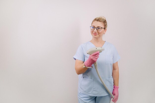 Portrait of the master of laser hair removal a woman in a blue\
robe holds a laser hair removal device in her hands