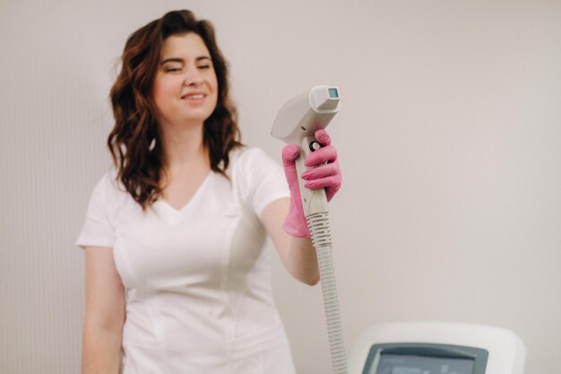 Portrait of the master of laser hair removal a woman in a white\
coat holds a laser hair removal devi