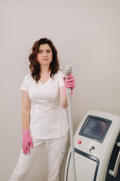 Portrait of the master of laser hair removal a woman in a white\
coat holds a laser hair removal device in her hands