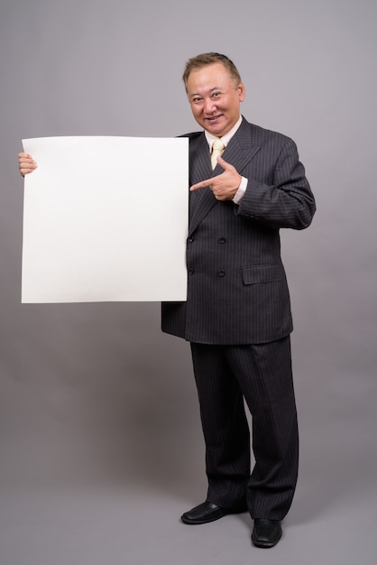 Portrait of mature Asian businessman against gray background