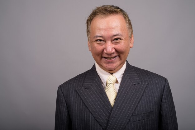 Portrait of mature Asian businessman against gray background