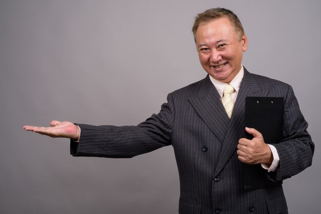 Portrait of mature Asian businessman against gray background