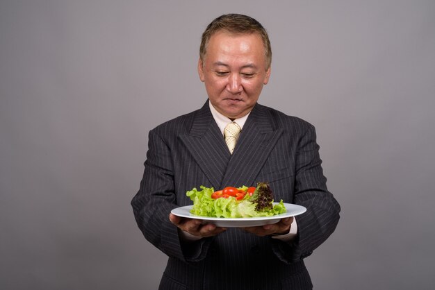 Portrait of mature Asian businessman against gray wall