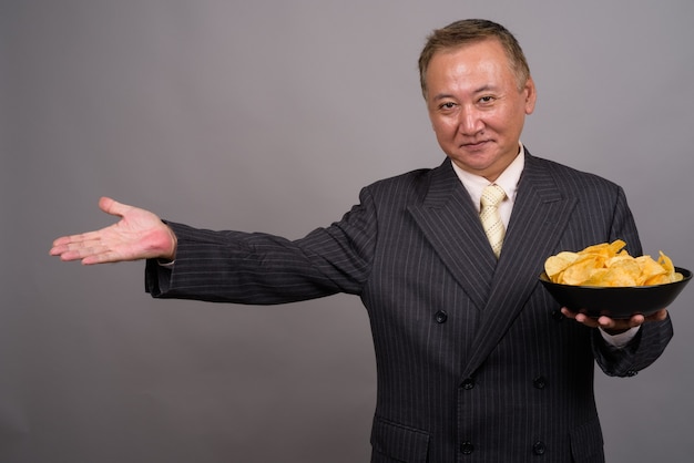 Portrait of mature Asian businessman against gray wall