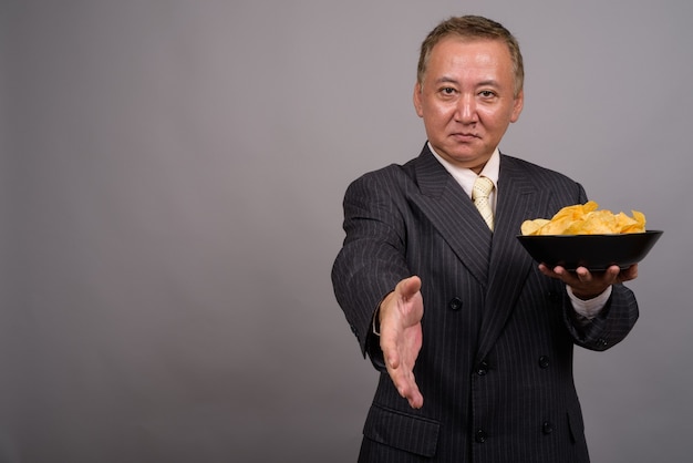 Portrait of mature Asian businessman against gray wall