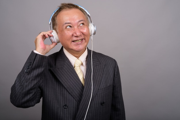 Portrait of mature Asian businessman against gray wall