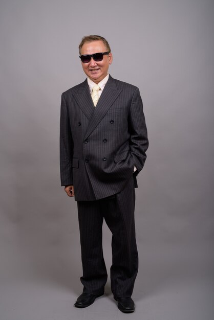 Portrait of mature Asian businessman against gray wall