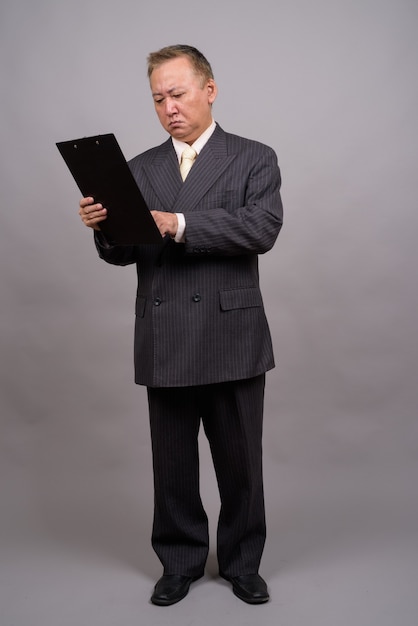 Portrait of mature Asian businessman against gray wall