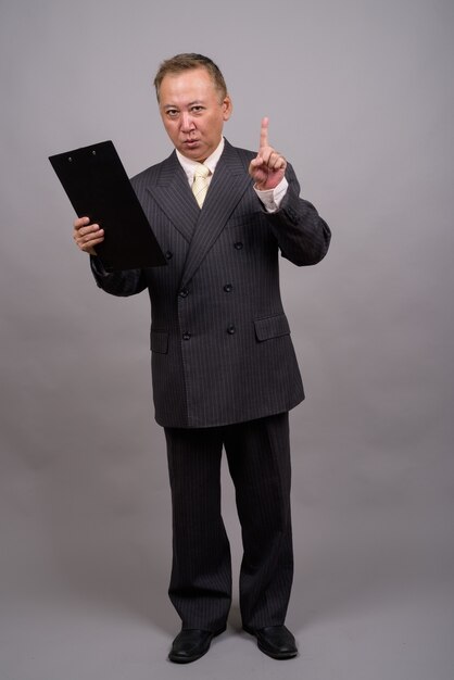 Portrait of mature Asian businessman against gray wall