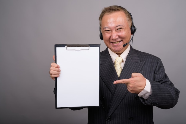 Портрет зрелого азиатского бизнесмена против серой стены