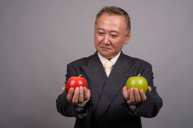 Portrait of mature Asian businessman against gray wall