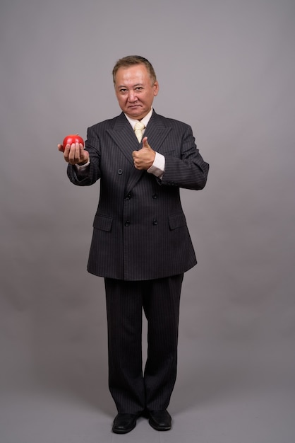 Portrait of mature Asian businessman against gray wall