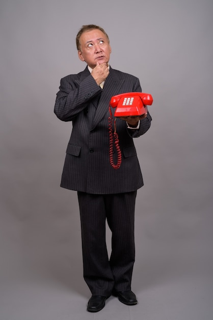 Portrait of mature Asian businessman against gray wall