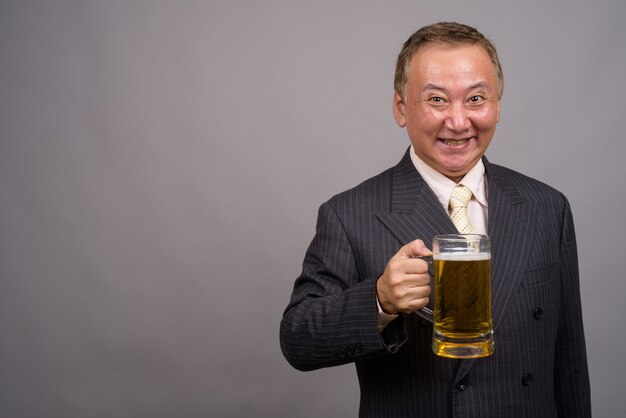 Portrait of mature Asian businessman against gray wall