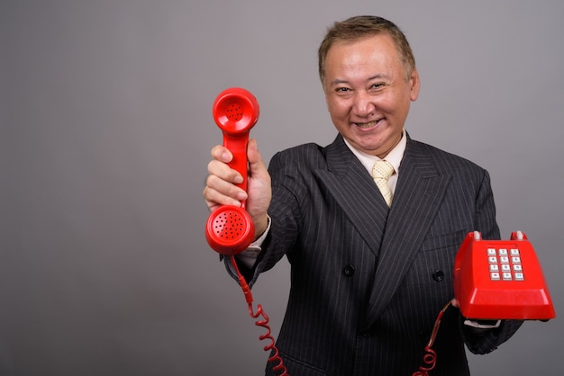 Portrait of mature Asian businessman against gray wall