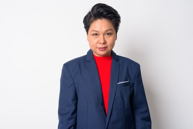 Portrait of mature Asian tomboy businesswoman wearing suit against white wall