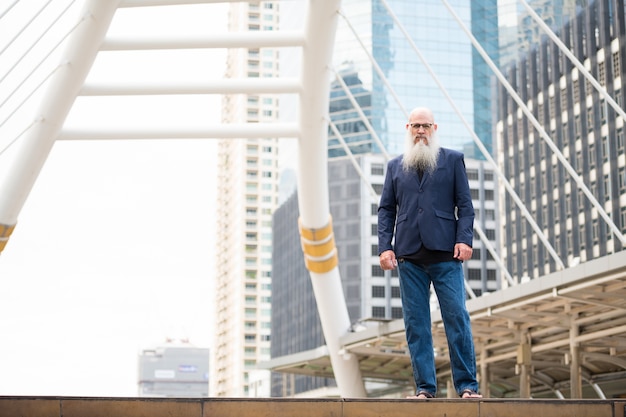 Portrait of mature bald businessman with long beard wearing eyeglasses in the city streets outdoors