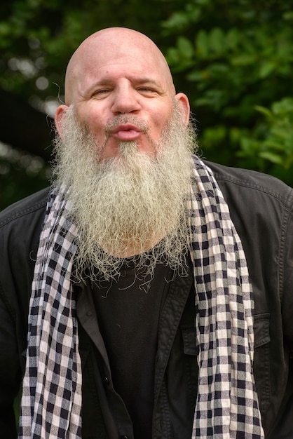 Portrait of mature bald hipster man with long beard at the park outdoors
