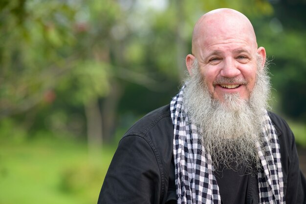 Portrait of mature bald hipster man with long beard at the park outdoors