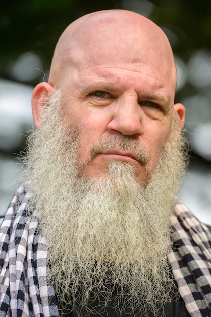 Portrait of mature bald hipster man with long beard at the park outdoors