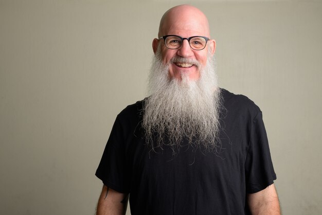 Portrait of mature bald man with long gray beard against white wall