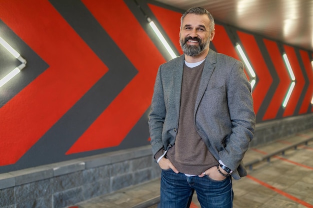 Portrait of a mature bearded businessman with a smile in a gray stylish jacket against a wall with