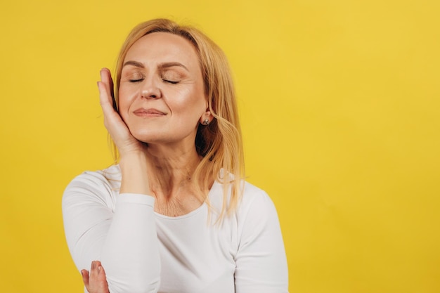 Portrait of mature beautiful woman holding hand near face on yellow background