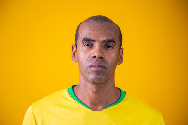 Portrait of mature black man in yellow brazilian outfit\
portrait of brazilian supporter on yellow background with free\
space for text