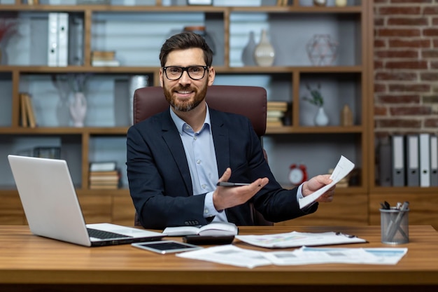 Photo portrait of mature businessman inside office at workplace man with documents smiling and looking at