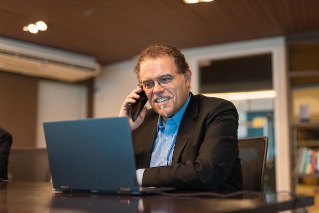 Portrait of mature businessman using laptop computer and mobile phone in office horizontal shot