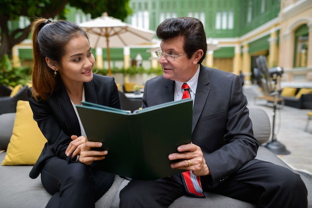 Portrait of mature businessman and young Asian businesswoman together as team diversity concept in the coffee shop