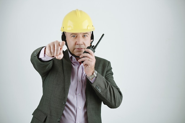 Portrait of mature construction manager or architect in hardhat pointing at camera while communicating through walkie-talkie