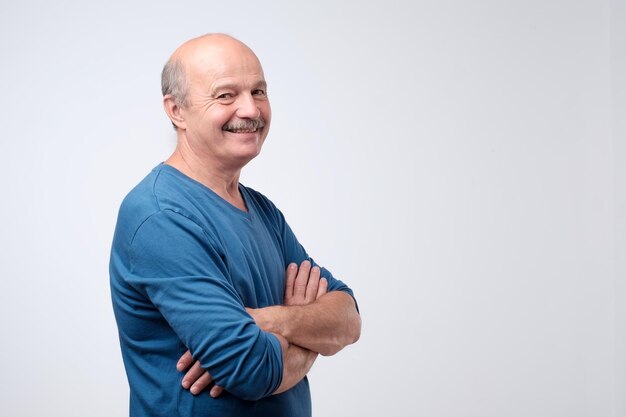 Portrait of mature european man with mustache in blue shirt having his arms crossed looking at camera