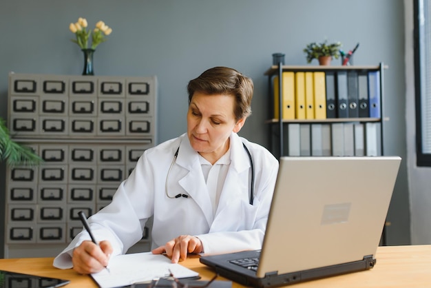 Portrait of mature female doctor in white coat at workplace