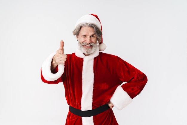 Portrait of mature gray-haired Santa Claus man in red costume pointing finger isolated on white in studio